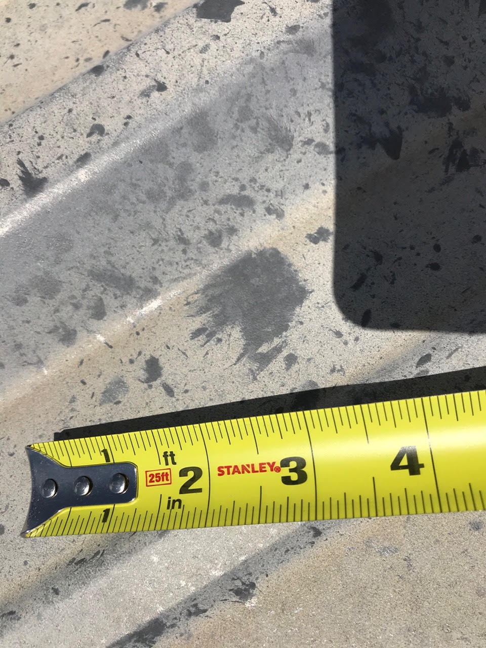 Tape measure beside hail splatter marks on a metal surface