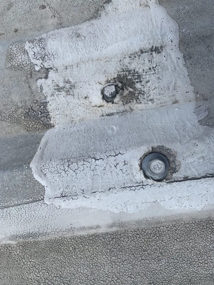 This close-up shows exposed fasteners and cracking in the white material around them and along a panel joint. We record the condition of each component rather than treating the roof as a single surface.