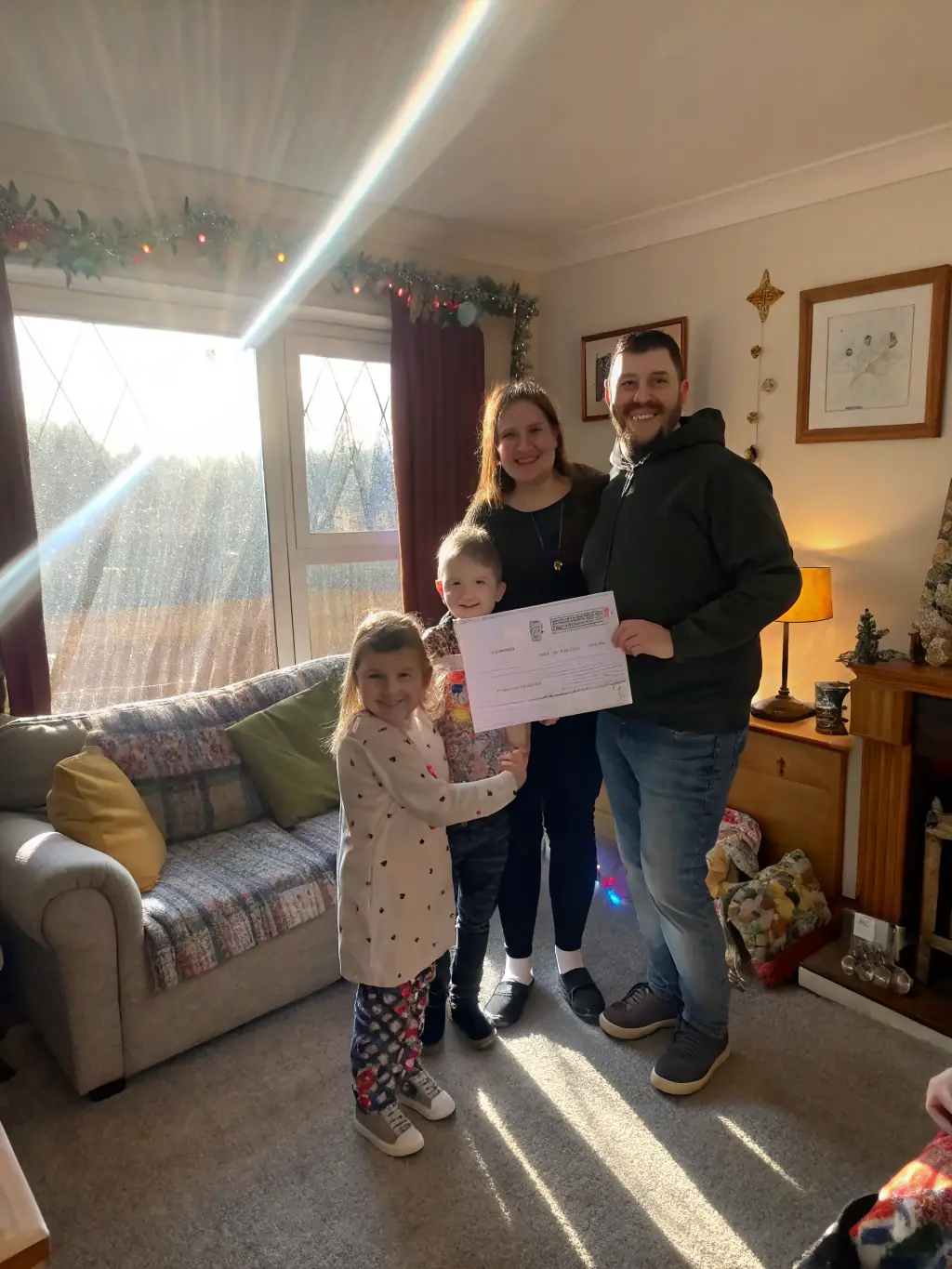 A photo of a family smiling in front of their fully restored home, holding a check representing their successful insurance claim settlement.